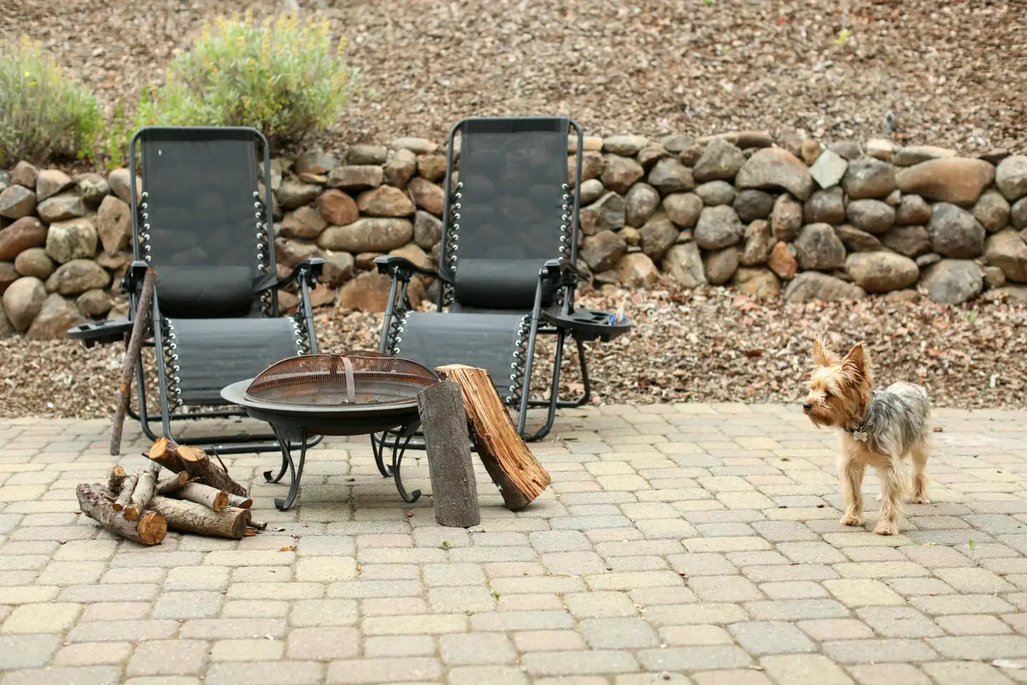 A paver patio laid in front of a stone retaining wall
